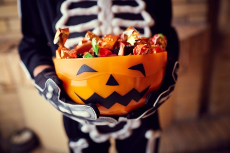 Boy in skeleton costume holding bowl full of candies.