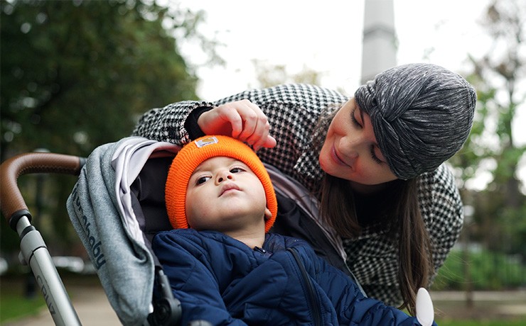 A woman leans over a stroller while speaking to her son.