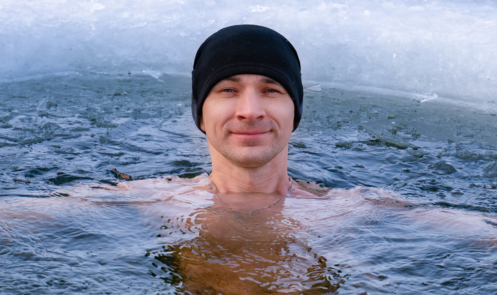 A man in a watch cap swims in cold water for the health benefits.