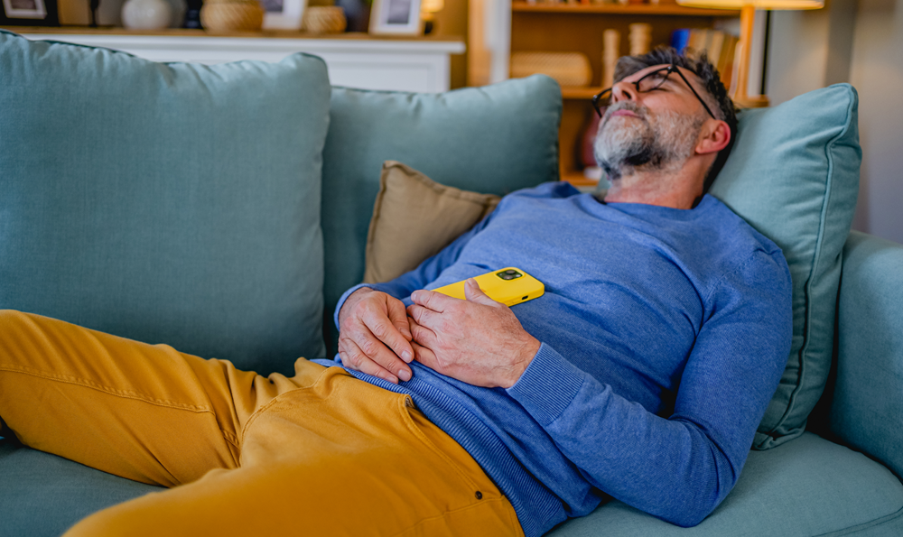 An adult man takes a nap on his couch.