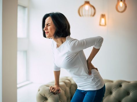 Woman with low back pain clasps her back.